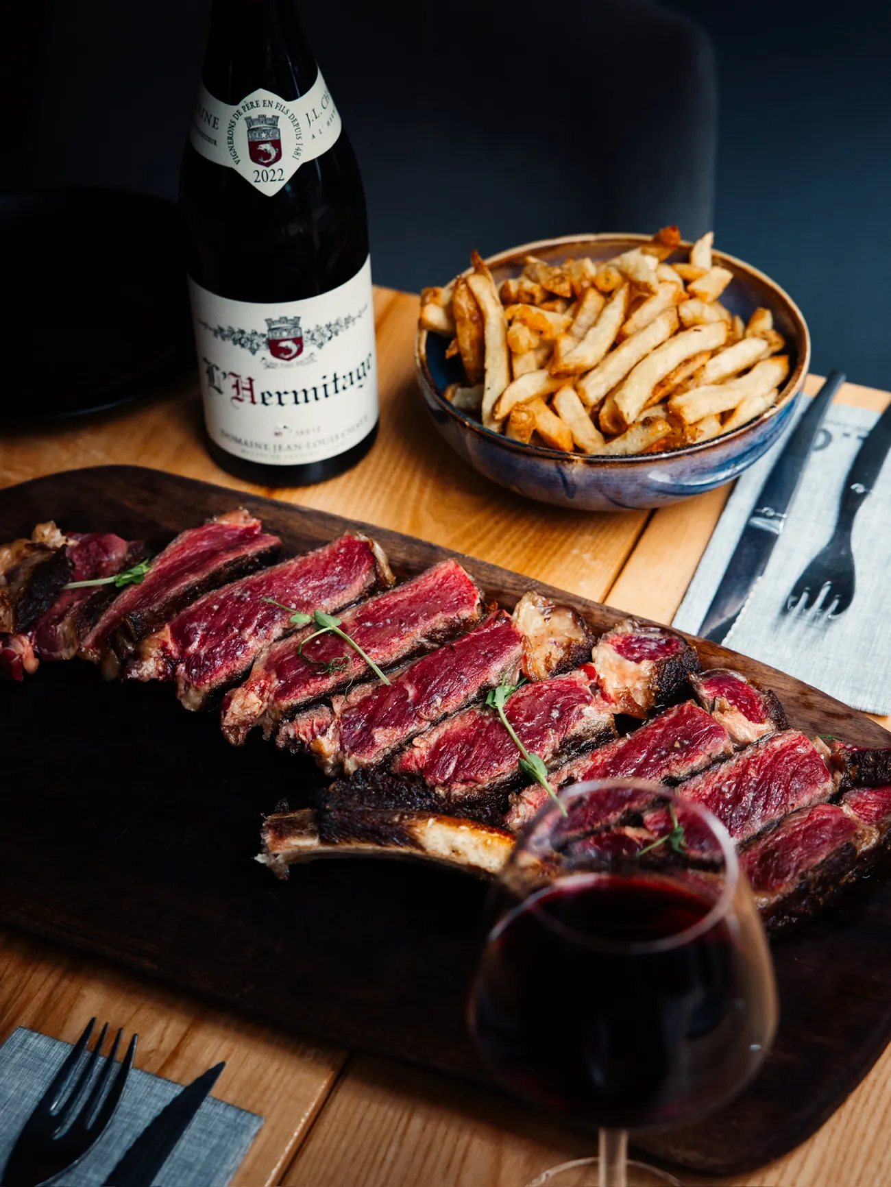 Côte de bœuf tranchée sur une planche, frites maison et verre de vin rouge