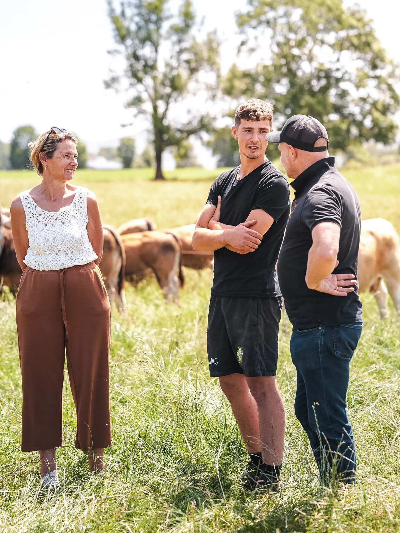Frédéric Bello discute avec deux éleveurs dans un pré, des vaches derrière eux