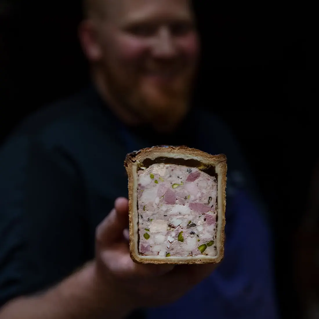 Jérémie Crauser, flou à l’arrière-plan, présente une tranche de pâté-croûte